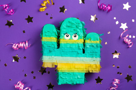 Cactus shaped pinata, streamers and glitter on purple background, flat layの写真素材