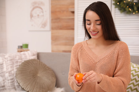 Happy young woman eating ripe tangerine at homeの写真素材
