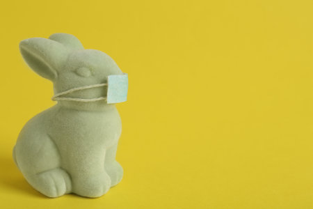 Cute bunny figure in protective mask on yellow background, space for text. Easter holiday during COVID-19 quarantineの写真素材