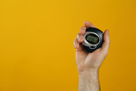 Man holding digital timer on yellow background, closeup. Space for textの写真素材