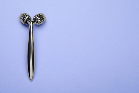 Metal face roller on lilac background, top view. Space for text