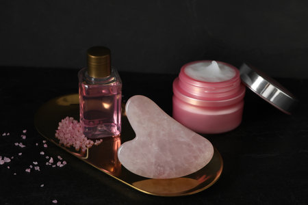 Rose quartz gua sha tool and cosmetic products on black tableの写真素材