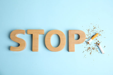 Broken cigarette near word Stop made with wooden letters on light blue background, flat lay. Quitting smoking conceptの写真素材