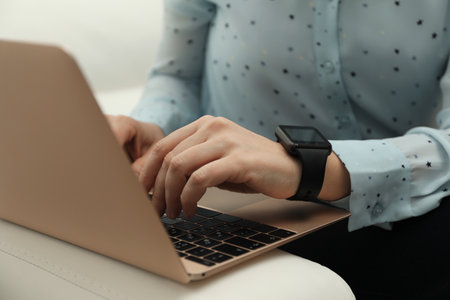 Mature woman with smart watch working on laptop indoors, closeupの写真素材