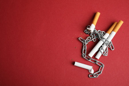 Cigarettes and chains on red background, flat lay with space for text. Quitting smoking conceptの写真素材