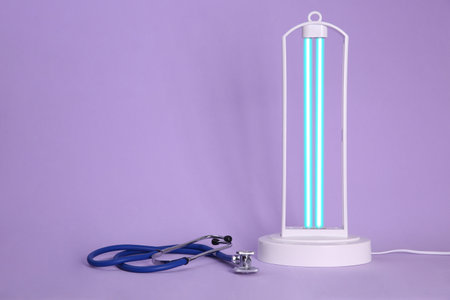Ultraviolet lamp and stethoscope on violet background, space for textの写真素材