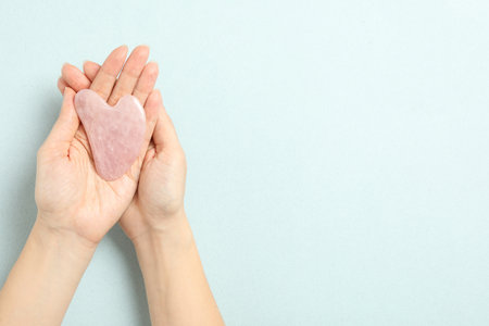 Woman with rose quartz gua sha tool on light blue background, closeup. Space for textの写真素材