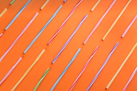 Colorful plastic straws for drinks on orange background, flat layの写真素材