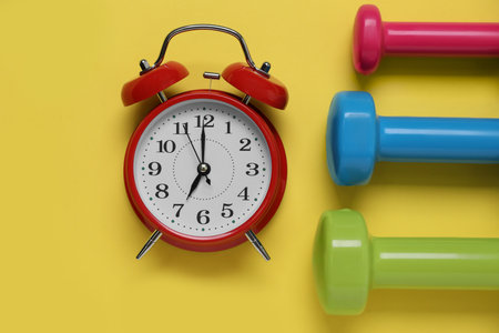 Alarm clock and dumbbells on yellow background, flat lay. morning exerciseの写真素材