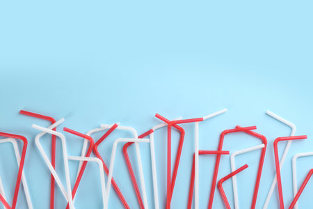 Colorful plastic drinking straws on light blue background, flat lay. Space for textの写真素材