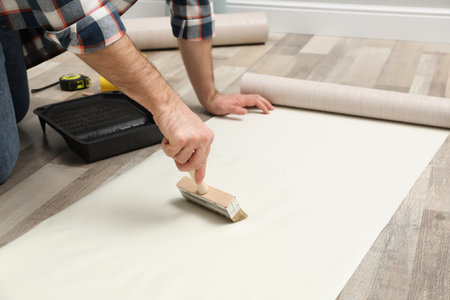 Man applying glue onto wall paper on floor, closeupの写真素材