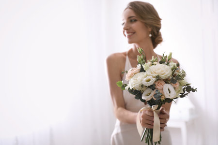 Young bride with beautiful wedding bouquet in room, focus on flowers. Space for textの写真素材