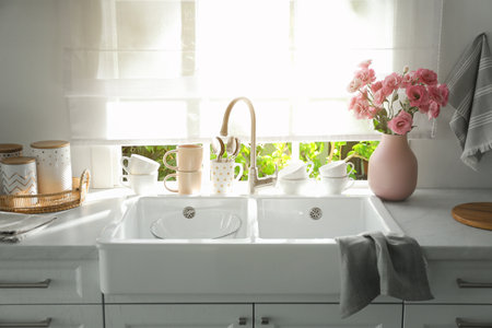 Vase with flowers on countertop near sink against window in kitchenの写真素材