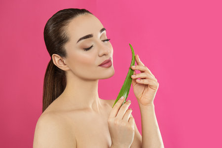 Young woman with aloe vera leaf on pink backgroundの写真素材