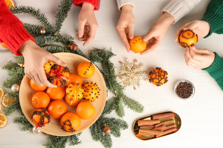 Friends decorating fresh tangerines with cloves at light table, top view. Making Christmas pomander ballsの写真素材
