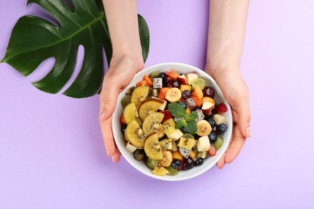 Woman with delicious exotic fruit salad on purple background, top viewの写真素材