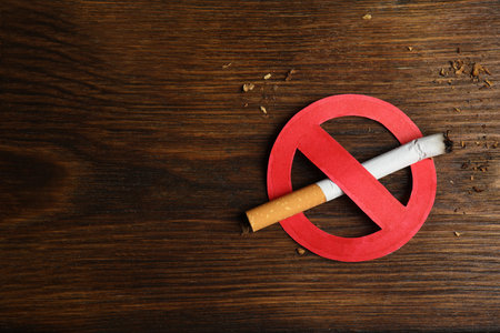 Cigarette with prohibition sign and space for text on wooden table, top view. Quitting smoking conceptの写真素材