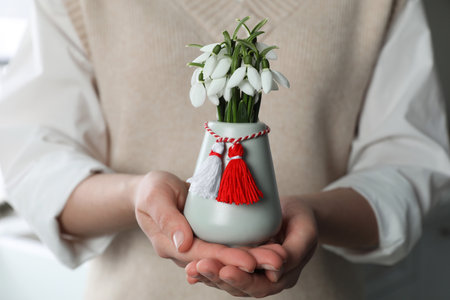 Woman holding vase with beautiful snowdrops and traditional martisor indoors, closeup. Symbol of first spring dayの写真素材