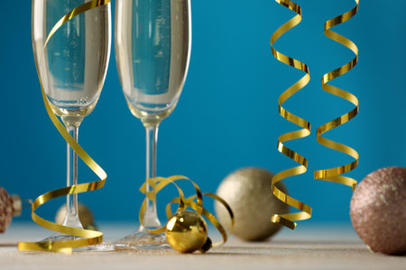 Glasses of champagne with serpentine streamers and Christmas ornaments on table against blue background, closeupの写真素材