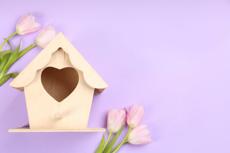 Beautiful bird house and pink tulips on violet background, flat lay. Space for textの写真素材
