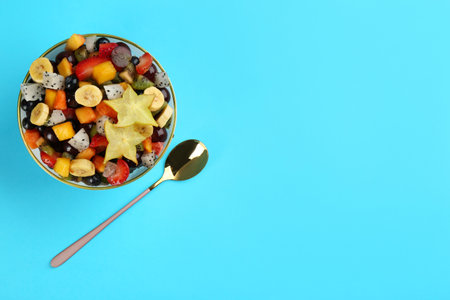 Delicious exotic fruit salad and spoon on light blue background, flat lay. Space for textの写真素材