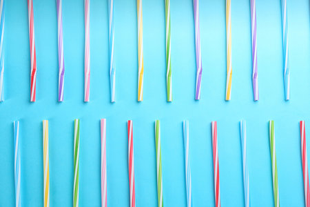 Colorful plastic drinking straws on light blue background, flat lay