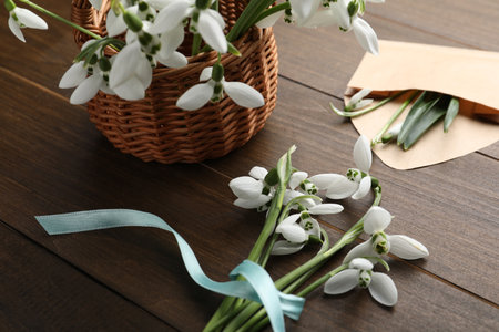 Beautiful snowdrops with wicker basket and envelope on wooden tableの写真素材