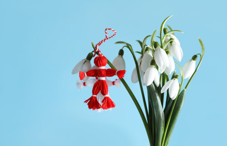 Traditional martisor and beautiful snowdrops on light blue background. Symbol of first spring dayの写真素材