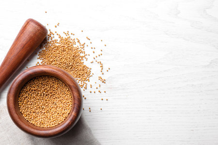 Mustard seeds with wooden mortar and pestle on white table, flat lay. Space for textの写真素材