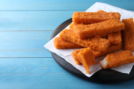Fresh breaded fish fingers served on light blue wooden table, space for textの写真素材