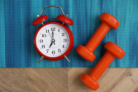 Alarm clock, yoga mat and dumbbells on wooden background, flat lay. morning exerciseの写真素材