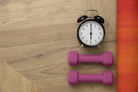 Alarm clock, yoga mat and dumbbells on wooden background, flat lay with space for text. morning exerciseの写真素材