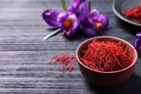 Dried saffron in bowl and crocus flowers on black wooden table, space for textの写真素材