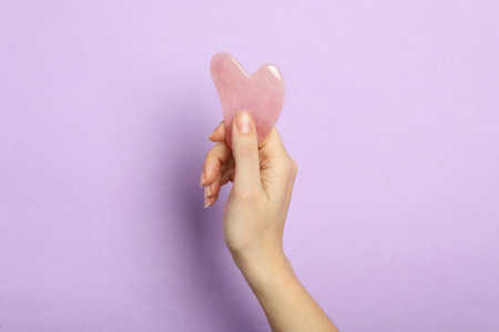 Woman with rose quartz gua sha tool on lilac background, closeupの写真素材