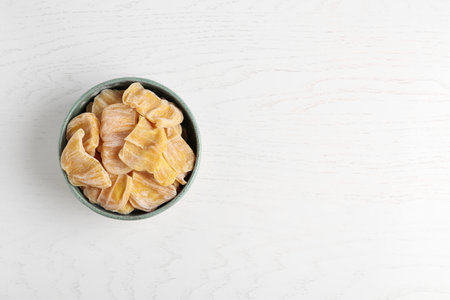 Delicious dried jackfruit slices in bowl on white wooden table, top view. Space for textの写真素材