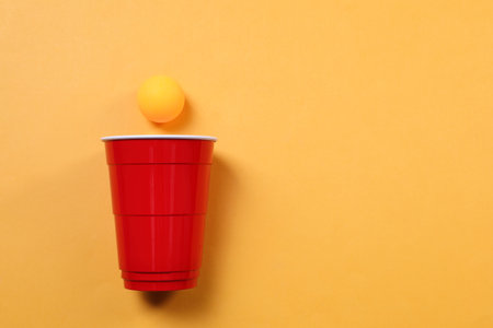 Plastic cup and ball on orange background, flat lay with space for text. beer pong gameの写真素材