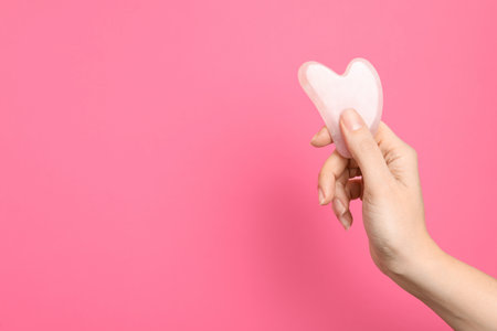 Woman with rose quartz gua sha tool on pink background, closeup. Space for textの写真素材