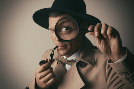 Male detective with smoking pipe looking through magnifying glass on beige backgroundの写真素材