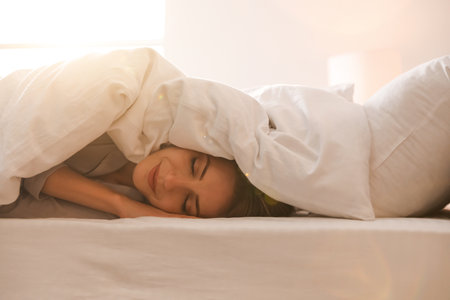 Woman under warm white blanket sleeping in bed indoorsの写真素材
