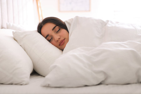 Young woman covered with warm white blanket sleeping in bed at homeの写真素材