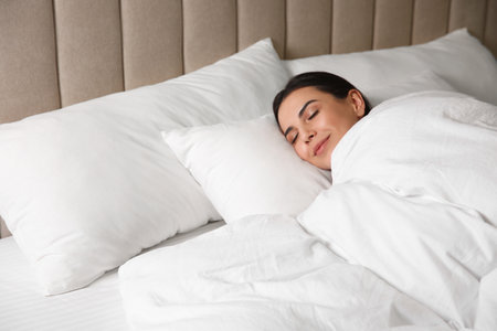 Young woman sleeping in bed covered with white blanketの写真素材