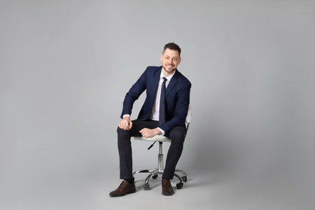 Handsome businessman sitting in office chair on gray backgroundの写真素材