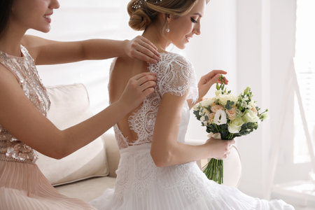 Young woman helping bride to put on wedding dress in roomの写真素材
