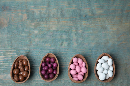 Broken chocolate Easter eggs with colorful candies on blue wooden table, flat lay. Space for text