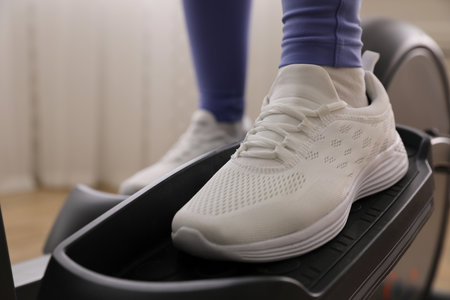 Woman using modern elliptical machine indoors, closeupの写真素材