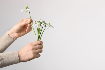 Woman holding beautiful bouquet of snowdrops on light background, closeup. Space for textの写真素材
