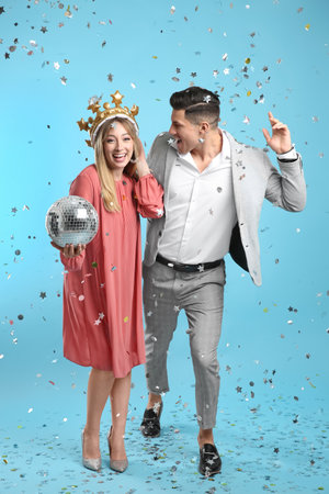 Happy couple with disco ball and confetti on light blue backgroundの写真素材
