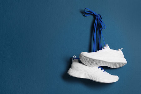 Pair of stylish shoes with laces hanging on blue wall, space for textの写真素材