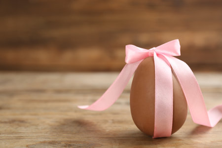 Sweet chocolate egg with pink bow on wooden table. Space for textの写真素材