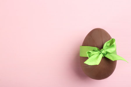 Sweet chocolate egg with green bow on pink wooden table, top view. Space for textの写真素材